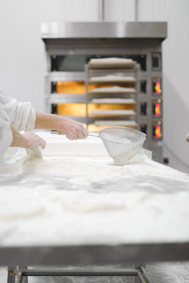 Commercial bakery deck oven with baker sifting flour in HACCP-compliant food production facility